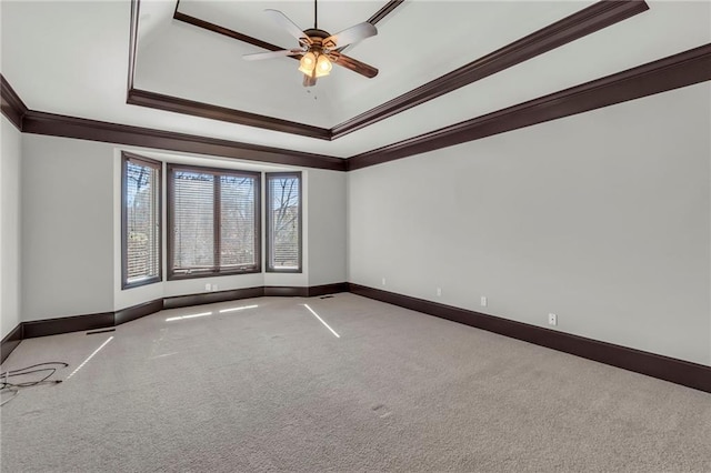 carpeted empty room with ornamental molding, a raised ceiling, a ceiling fan, and baseboards