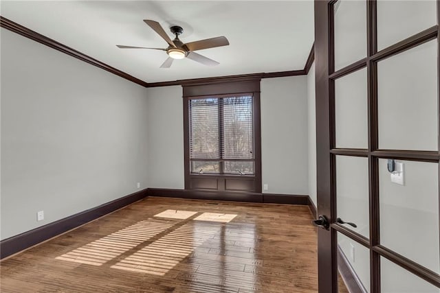 empty room with french doors, ornamental molding, a ceiling fan, wood finished floors, and baseboards