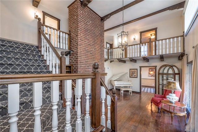 stairway featuring a chandelier, beam ceiling, wood-type flooring, and a high ceiling