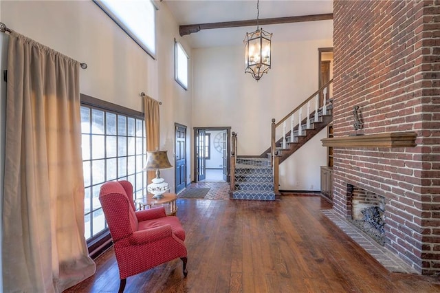 foyer featuring wood-type flooring, an inviting chandelier, a brick fireplace, beamed ceiling, and stairs