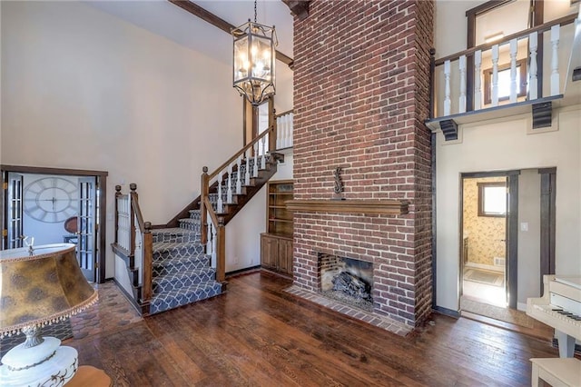 foyer entrance with baseboards, a towering ceiling, stairway, hardwood / wood-style floors, and a brick fireplace