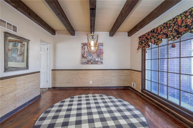 unfurnished dining area with a wainscoted wall, beam ceiling, visible vents, and wood finished floors