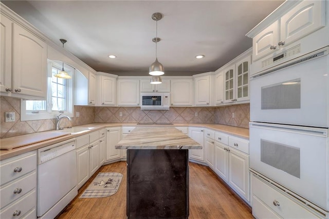 kitchen featuring white appliances, decorative light fixtures, a sink, and light wood-style flooring