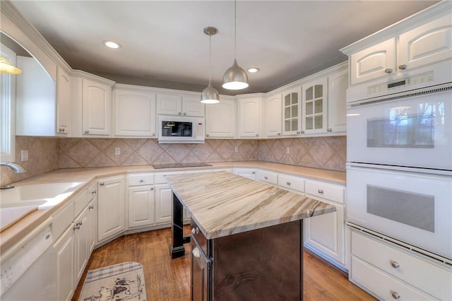 kitchen featuring white appliances, a sink, white cabinets, hanging light fixtures, and light wood-type flooring