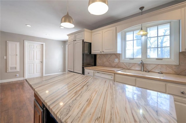 kitchen featuring decorative backsplash, freestanding refrigerator, white cabinetry, pendant lighting, and a sink