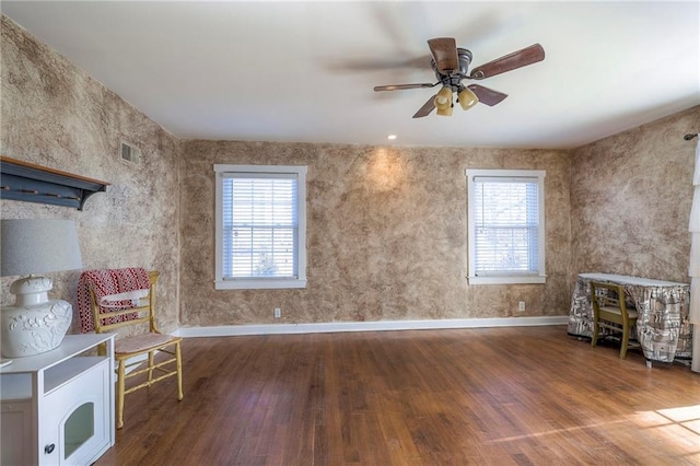 living area with a ceiling fan, visible vents, baseboards, and wood finished floors