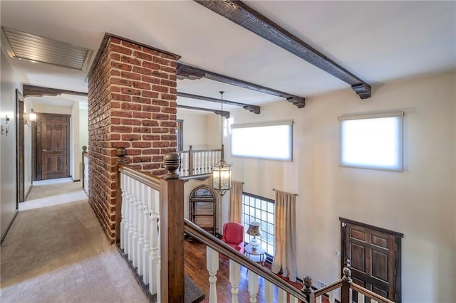 hall featuring carpet flooring, beamed ceiling, and an upstairs landing