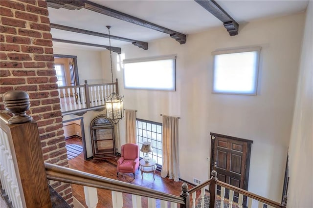 staircase with a healthy amount of sunlight, a chandelier, beam ceiling, and wood finished floors