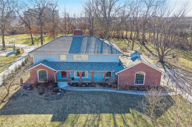 view of front facade with roof with shingles, a chimney, a porch, and brick siding