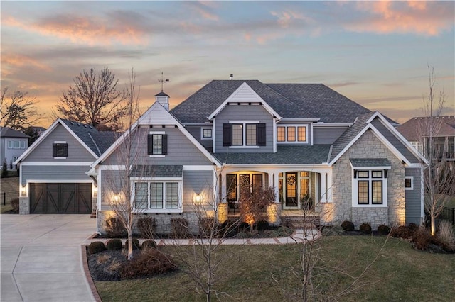 view of front of property featuring a shingled roof, concrete driveway, stone siding, a chimney, and a front lawn