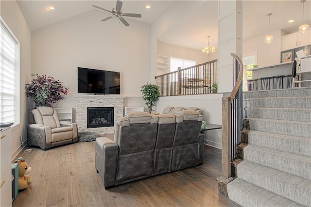 living room featuring stairs, a stone fireplace, vaulted ceiling, and wood-type flooring