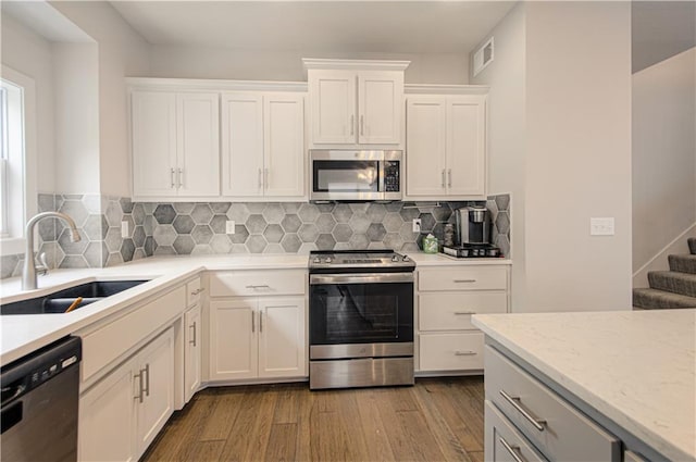 kitchen with stainless steel appliances, visible vents, white cabinets, a sink, and wood finished floors