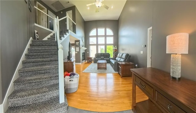 interior space with a fireplace, a high ceiling, a ceiling fan, wood finished floors, and baseboards