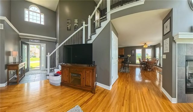 living area with a high ceiling, wood finished floors, baseboards, stairway, and a tiled fireplace