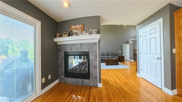 unfurnished living room featuring a tile fireplace, baseboards, and wood finished floors