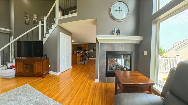 living room featuring light wood finished floors, baseboards, a fireplace, and stairway