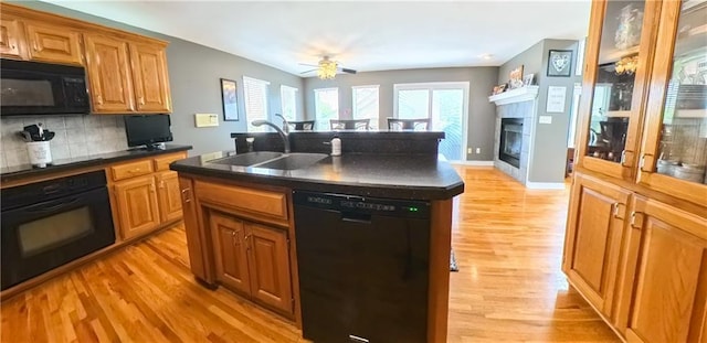 kitchen featuring black appliances, a glass covered fireplace, dark countertops, and a sink