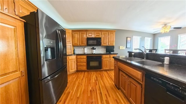 kitchen with a sink, light wood-type flooring, brown cabinets, black appliances, and dark countertops