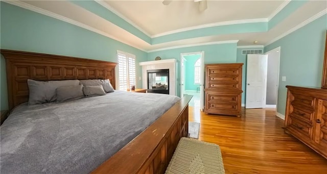 bedroom with ornamental molding, light wood-type flooring, a raised ceiling, and visible vents