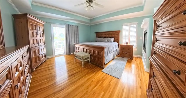 bedroom with light wood-type flooring, access to outside, multiple windows, and a raised ceiling