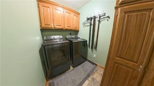 clothes washing area featuring washing machine and dryer, cabinet space, and baseboards