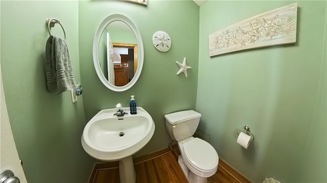 half bath with toilet, baseboards, a sink, and wood finished floors