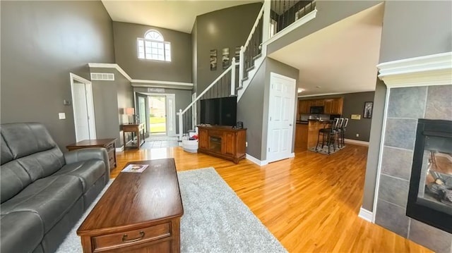 living room featuring light wood finished floors, visible vents, stairway, a tiled fireplace, and baseboards