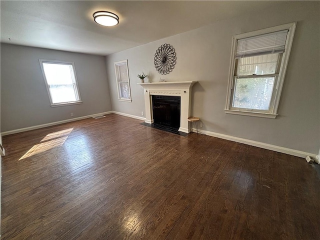 unfurnished living room with dark wood-style floors, a fireplace with flush hearth, visible vents, and baseboards