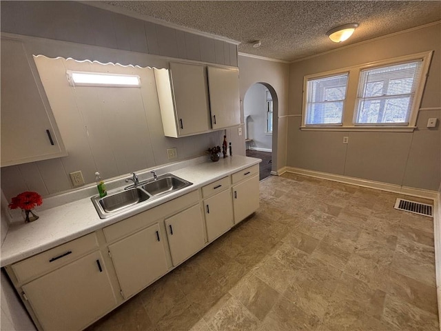 kitchen with arched walkways, a sink, visible vents, white cabinetry, and light countertops