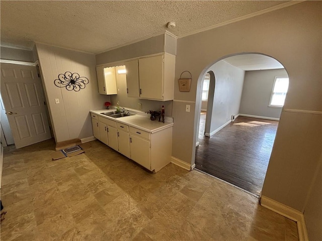 kitchen with arched walkways, a sink, white cabinetry, light countertops, and crown molding