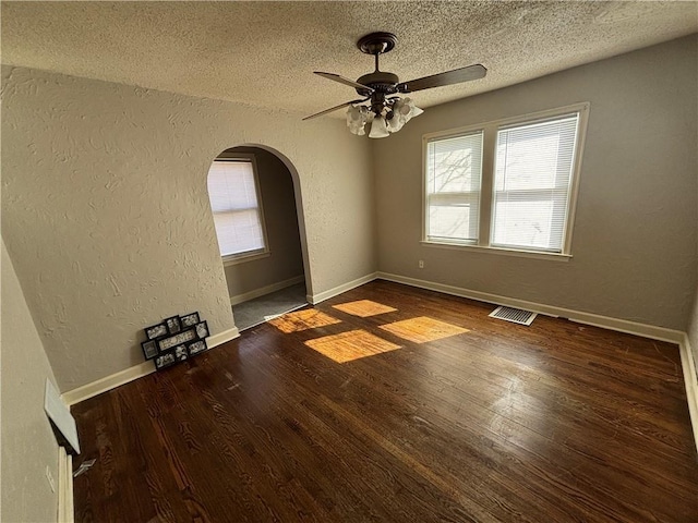 unfurnished room with arched walkways, a textured wall, a textured ceiling, wood finished floors, and visible vents