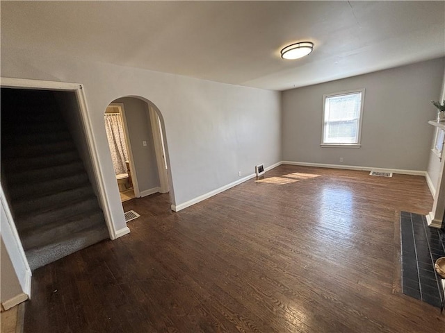 empty room with dark wood-type flooring, arched walkways, visible vents, and stairway