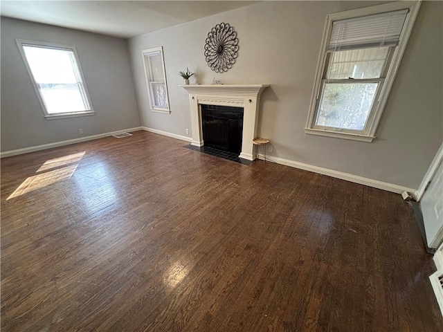 unfurnished living room with dark wood-style flooring, a fireplace with flush hearth, visible vents, and baseboards