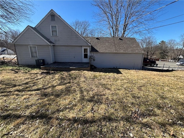 back of property with a shingled roof, a lawn, a deck, and fence