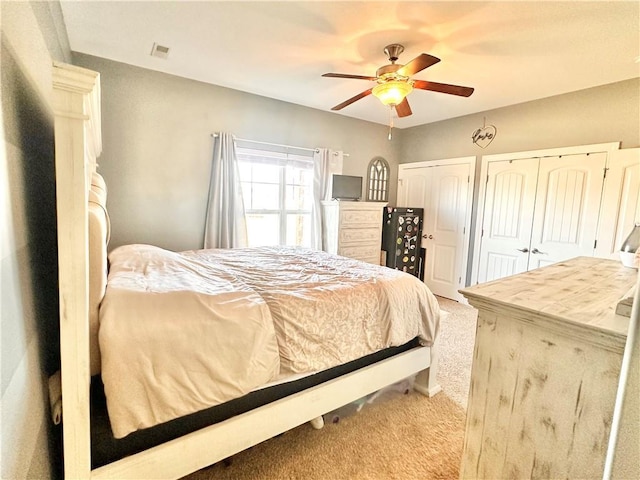 carpeted bedroom featuring ceiling fan, visible vents, and multiple closets