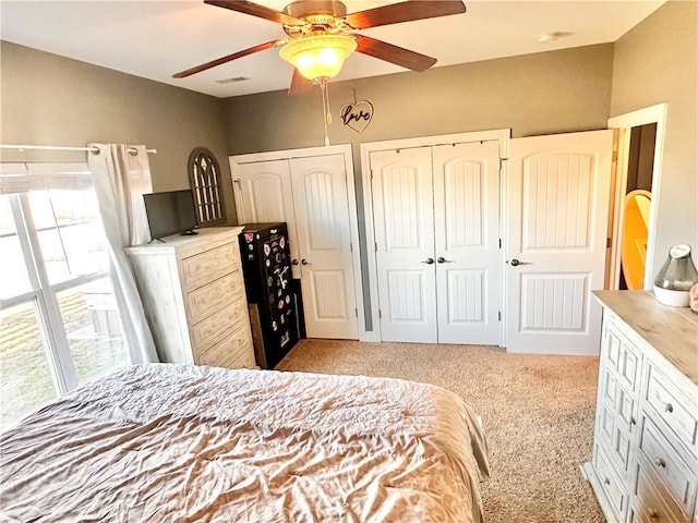 bedroom with a ceiling fan, visible vents, multiple closets, and light colored carpet