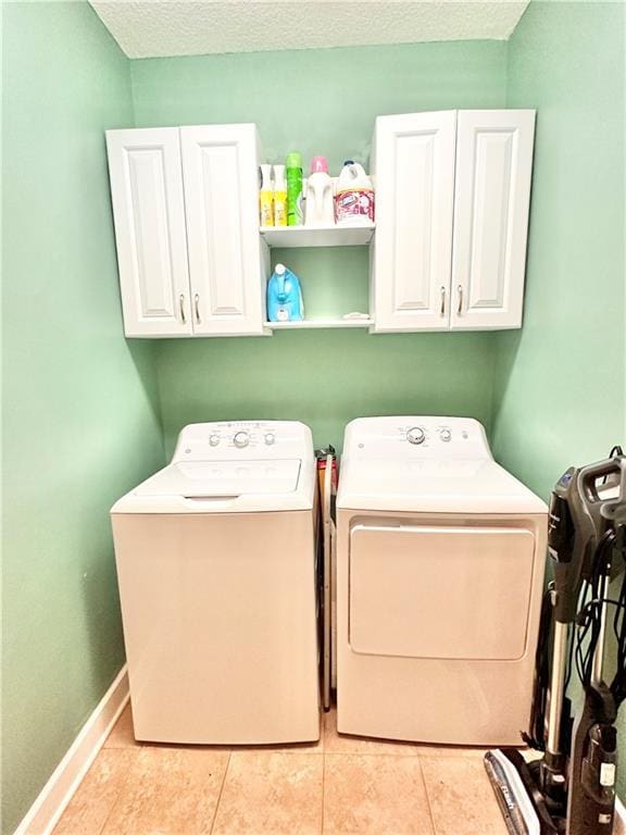 laundry room with light tile patterned floors, a textured ceiling, separate washer and dryer, baseboards, and cabinet space