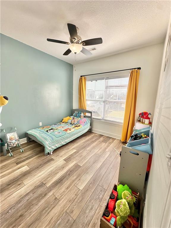 bedroom with baseboards, visible vents, ceiling fan, wood finished floors, and a textured ceiling