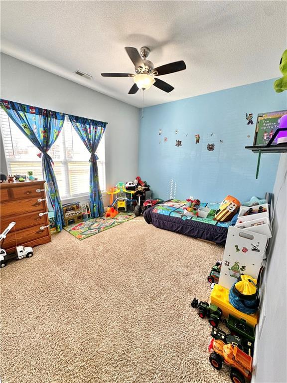 bedroom with a textured ceiling, carpet, visible vents, and a ceiling fan