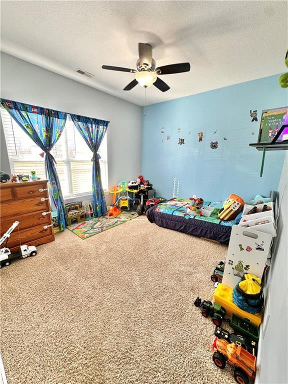 playroom with a textured ceiling, ceiling fan, carpet flooring, and visible vents