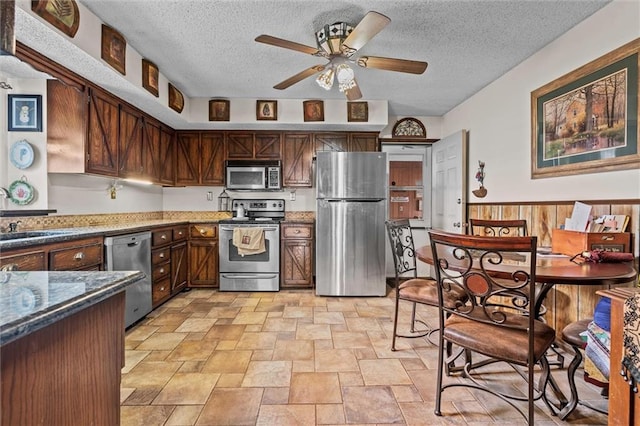 kitchen with ceiling fan, a textured ceiling, a sink, appliances with stainless steel finishes, and dark stone counters