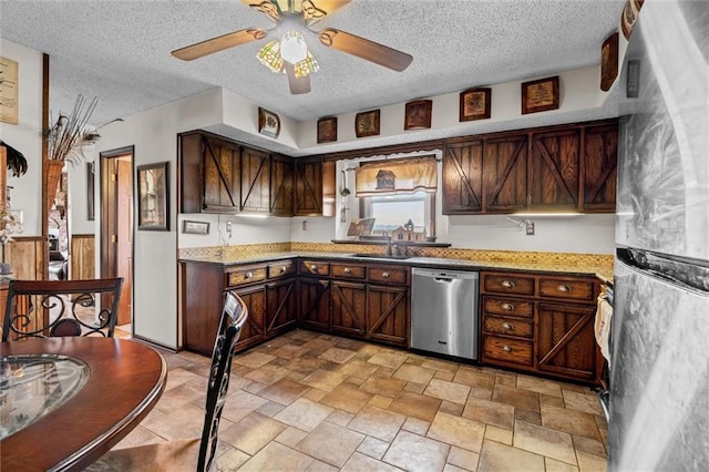 kitchen with a wainscoted wall, a textured ceiling, appliances with stainless steel finishes, and a sink