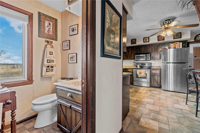 kitchen with stainless steel appliances, a ceiling fan, stone finish floor, a textured ceiling, and dark brown cabinets