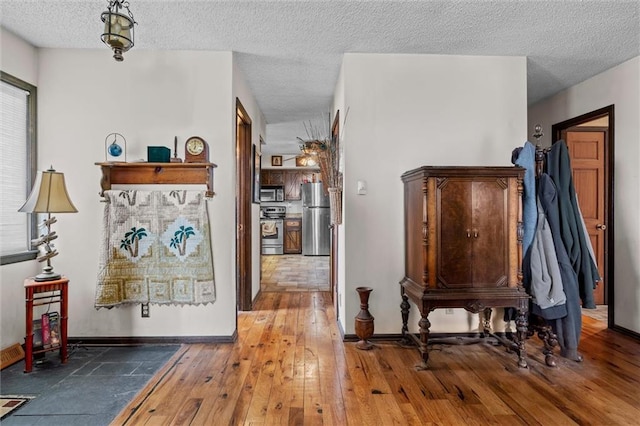 hall featuring a textured ceiling, baseboards, and hardwood / wood-style floors