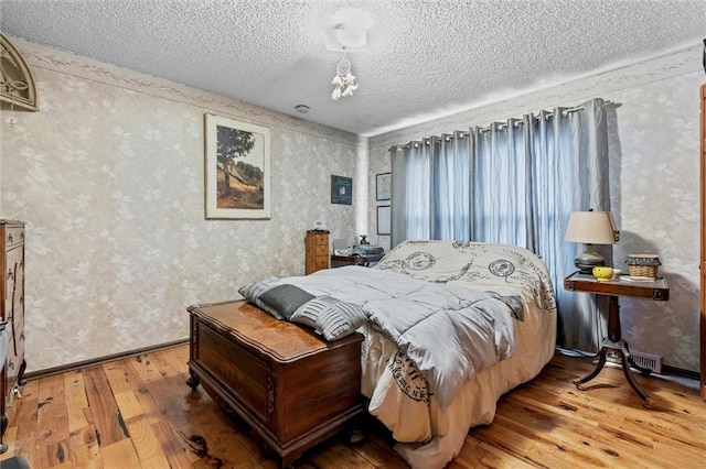 bedroom with wallpapered walls, a textured ceiling, and hardwood / wood-style floors