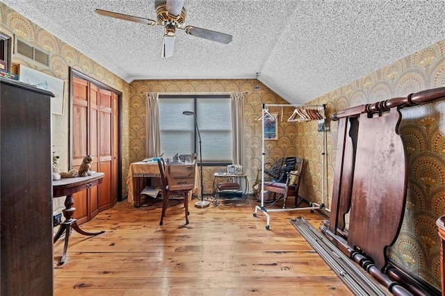 office space with wallpapered walls, visible vents, hardwood / wood-style floors, vaulted ceiling, and a textured ceiling