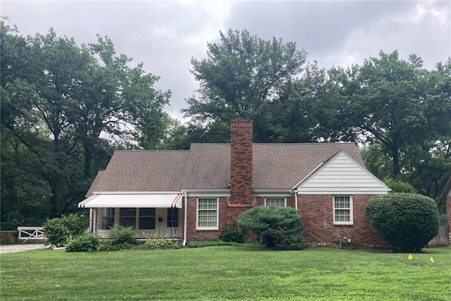 view of front of home featuring a front lawn, a chimney, a shingled roof, and brick siding