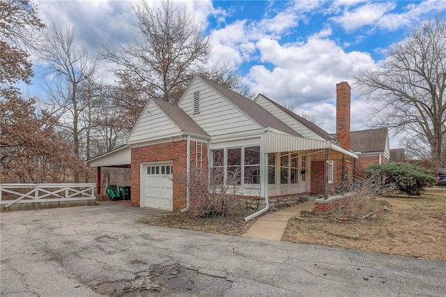 view of front of house with a garage, driveway, a chimney, fence, and brick siding