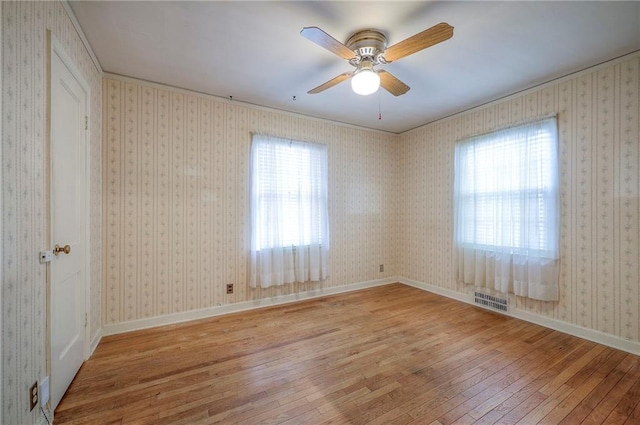 empty room featuring baseboards, hardwood / wood-style flooring, visible vents, and wallpapered walls