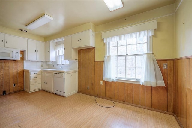 kitchen with light countertops, white appliances, wood walls, and white cabinets